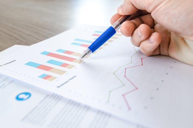 A hand with a pen tapping some charts on a piece of paper